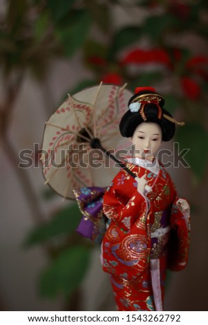 Japanese traditional doll in red kimono with a plant as background