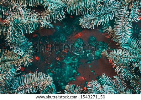 Winter holidays creative greeting card. Fir tree sprigs circle frame on red and emerald green paint background. Copy space.