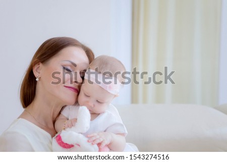 Cute girl baby in a tender embrace of her mother on the couch. Shot at home