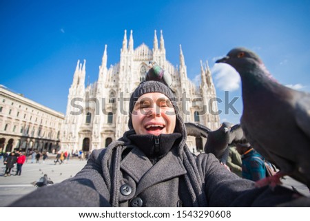 Winter travel, vacations and birds concept - Handsome male tourist with funny pigeons making selfie photo in front of the famous Duomo cathedral in Milan.