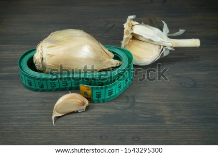 Elephant garlic (Allium ampeloprasum) and regular garlic cloves and tape measure on a rustic wooden table