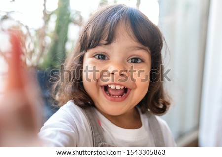Portrait of an adorable little girl taking a selfie while playing in her living room at home