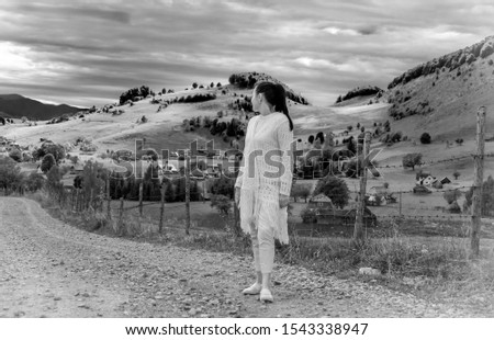 Young woman traveller admiring panoramic view of autumn.Girl dressed in white in a beautiful country decor. Plains, hills and mountains on the farm. Admire the beautiful farm scenery. B/W photography.