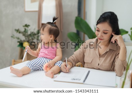 Little assistant. Little baby girl using pen while sitting on office desk with her mother in office