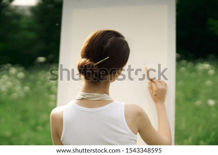 young easel woman paints a picture on white canvas