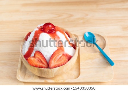 Bingsu or shaved ice in a wooden cup decorated with strawberries topped with strawberry sauce