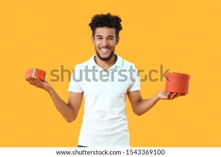 Portrait of happy African-American man with gifts on color background
