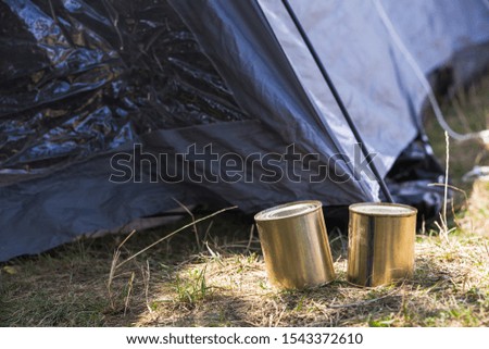 Canned beef stands on the forest ground near a blue tent at sunny day. Close-up outdoor photo. Basic hike food  ingredient