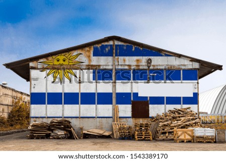 Close-up of the national flag of Uruguay
 painted on the metal wall of a large warehouse the closed territory on a summer day. The concept of storage of goods, entry to a closed area, tourism