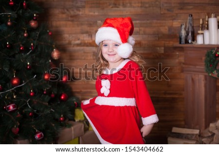 Beautiful little blonde baby girl, has happy fun cheerful smiling face, blue eyes, red Christmas hat Santa Claus, gift. Portrait holiday. Close up. Winter background. Family portrait.