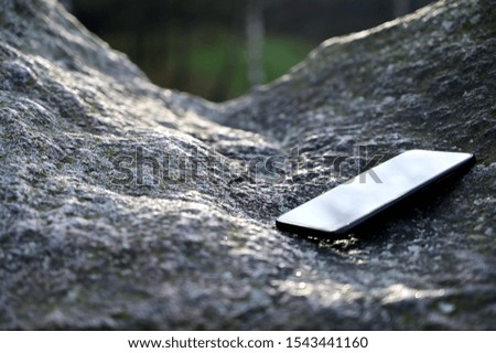 The concept of lost time. Photo of a smartphone on a natural stone. Autumn Park. Image of nature, forest, landscape.