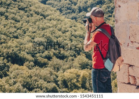 Hiker in mountains taking a photo. Young man with backpack and digital photo camera.