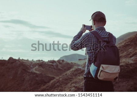 Man on top of a hill taking a photo on smartphone. Photo tour concept.