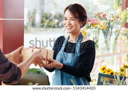 Cheerful young Asian florist giving gift box to client sho ordered it online
