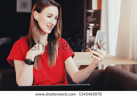 Female looking at screen of smartphone, selecting songs for playlist and listening to music using wireless earphones. Young woman watching webinar on mobile phone. Girl using digital content for work.