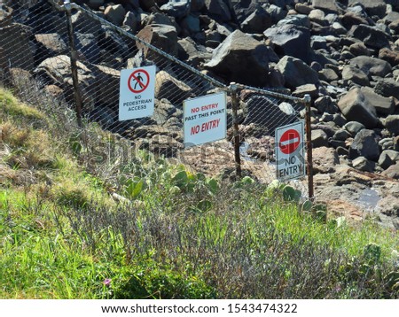 Diagonal metal mash fence with keep out signs running down hill