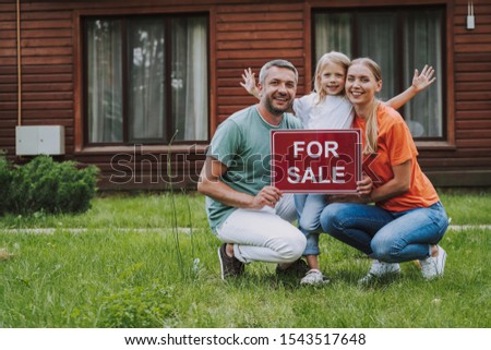 Smiling little girl and her parents holding for sale card outside the house