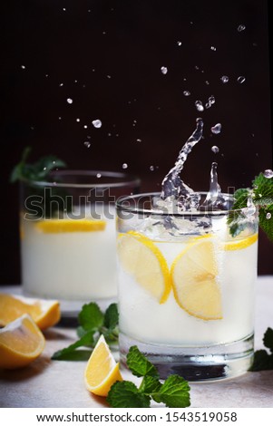 Summer cold drink closeup with drink splashing. Fresh cocktail with lemon, mint and ice in glass on black background. Studio shot in freeze motion, drops in liquid splash. 