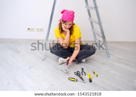 A young woman is thinking about repair questions laying out construction tools in front of her