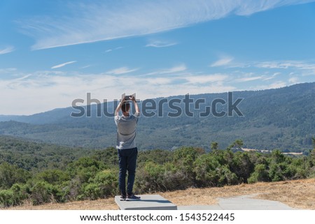 Rear view of young Caucasian man taking photo of nature San Jose mountain landscape from viewpoint, rest area near U.S. 101 Highway. Back of traveler using smart phone take photo