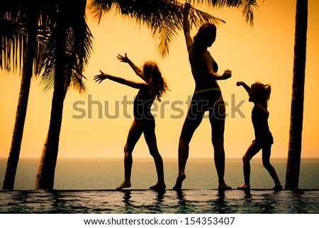 silhouette of a woman and two young girls standing by the pool on sea background
