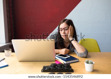 Female worker feeling lack of motivation , tired and sad , thinking about problem while sitting at desktop with open laptop computer in modern co-working space 