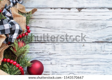 Christmas Day background with holiday trimmings of pine tree branches, ornaments, black and white buffalo check ribbon, burlap and red bead garland. Top view with copy space available.