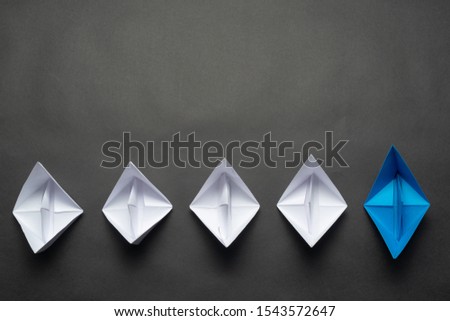 Row of paper ships on black background. Leadership concept with blue paper ship leading among white. Individual motivation and direction. Social marketing layout with copy space.