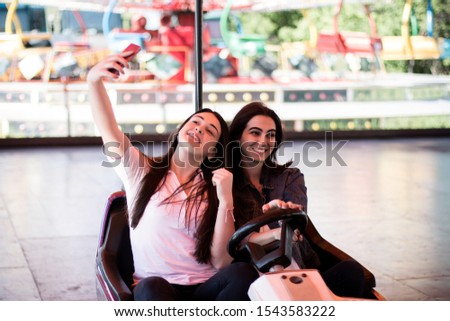 Two young women having a bumper car ride and taking a selfie with a phone.