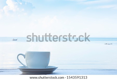 Hot coffee in a white cup with saucer on a wooden table Background blurry boat and sea.
