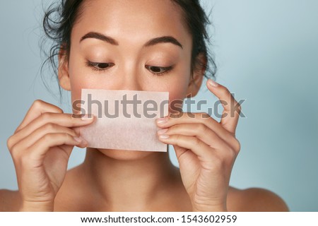 Skin care. Woman holding facial oil blotting paper portrait. Closeup of beautiful asian girl model with natural face makeup looking at oil absorbing tissue, beauty product.  Royalty-Free Stock Photo #1543602959