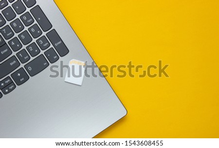 Laptop and SD memory card on yellow paper background. Modern gadgets. Top view