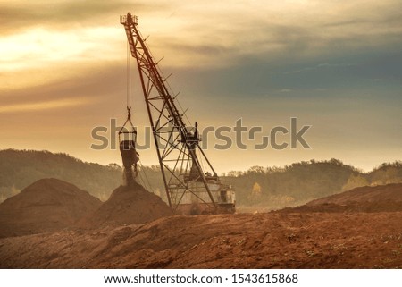 Red clay quarry with old heavy excavator for digging during bright sunrise. 