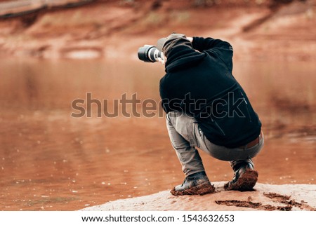 Man photographer holding camera with long lens and taking pictures in outdoors during sunny autumn day.