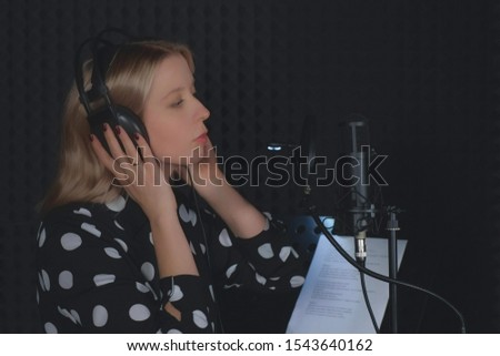 Portrait of young woman singer putting on headphones and starting to sing in microphone listening and recording music song in professional sound studio. Creating audio music composition.