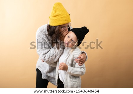 A young and energetic mother hugs and kisses her son on an orange background