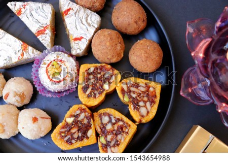 Assorted Indian sweets or Mithai, Rava laddo, besan ladu, dry fruits sweets in black plate along with Happy Diwali labeled chocolates for Diwali festivals, selective focus, copy space
