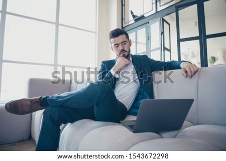 Portrait of his he nice rich attractive focused bearded guy investor financier wearing jacket sitting on divan using laptop reading browsing web surfing in modern luxury interior room indoors