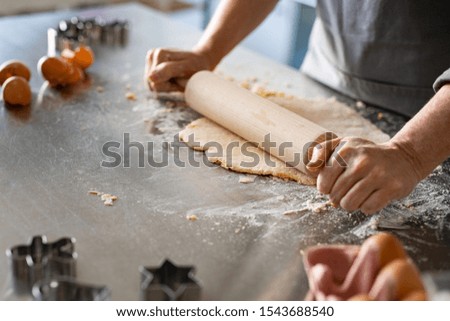 Closeup of woman hands holding rolling pin to flatten dough on kitchen counter. Old woman rolling dough for cookie on platform at home with ingredient around. Mature woman cooking christmas cookies.