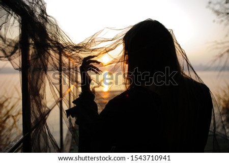silhouette of female hand with long nails on sunrise background through black fatin. halloween