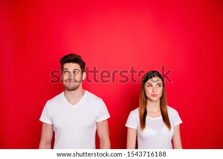 Photo of puzzled sly interested girlfriend boyfriend looking up in search of answers to questions with girl lips pouted and man stubble isolated in white t-shirts over vibrant color background