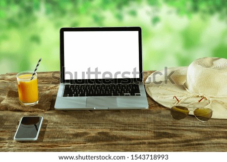 Blank screens of laptop and smartphone on a wooden table outdoors with nature on background, mock up. Glasses and fresh juice near by. Concept of creative workplace, business, freelance. Copyspace.