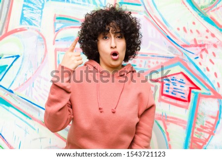 young pretty afro woman pointing at camera with an angry aggressive expression looking like a furious, crazy boss against graffiti wall