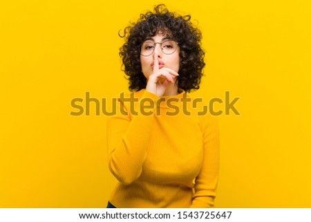 young pretty afro woman asking for silence and quiet, gesturing with finger in front of mouth, saying shh or keeping a secret