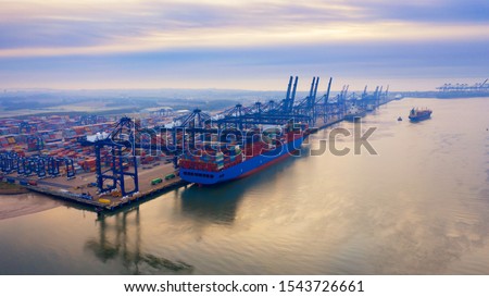 Aerial photograph of Felixstowe container port in the early morning autumn mist, a cargo ship being loaded, rows of stacked multi-colored containers, and loading gantries stretching off into the mist Royalty-Free Stock Photo #1543726661