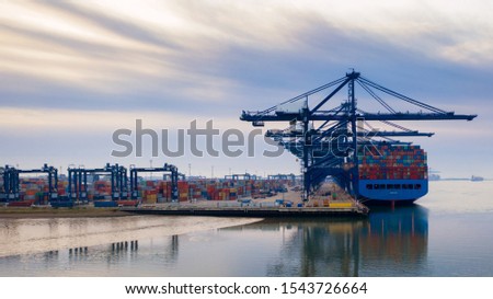 Aerial photograph looking through the line of loading gantrys in the early morning mist at Felixstowe container port. rows of stacked containers disappear into the distance early morning clouds streak Royalty-Free Stock Photo #1543726664