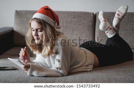 Portrait of pretty girl on the sofa at Christmas writes plans for the new year