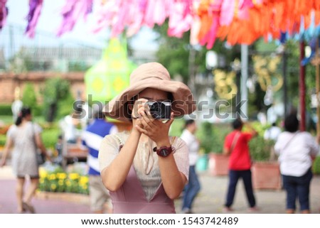 Asian woman with a camera stands to take pictures of people around her.​ color​ful​ background.