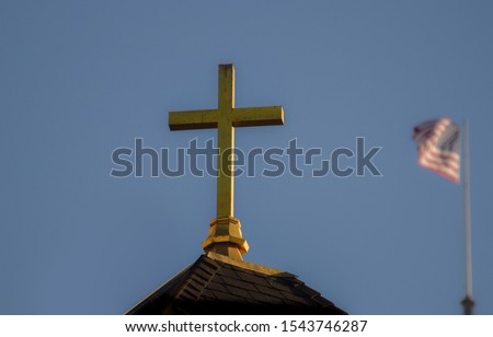 Golden cross on rooftop with waving American flag on rooftop behind it