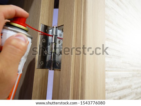 A man lubricates door hinges with oil. Royalty-Free Stock Photo #1543776080